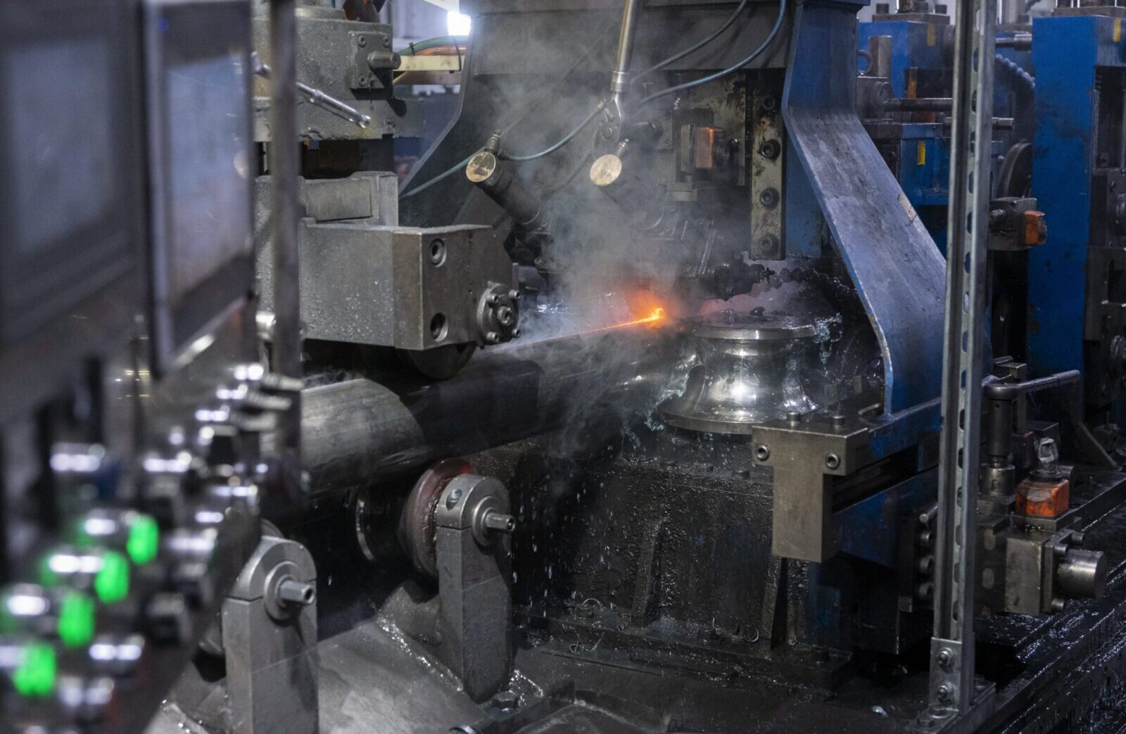 Tubing process machine welding metal with sparks and coolant in a factory.